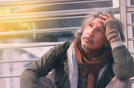 Homeless man is sitting down on walkway in town.He is very sadly and unhappy.poverty,despair,Photo Sympathetic and hope concept.の写真素材