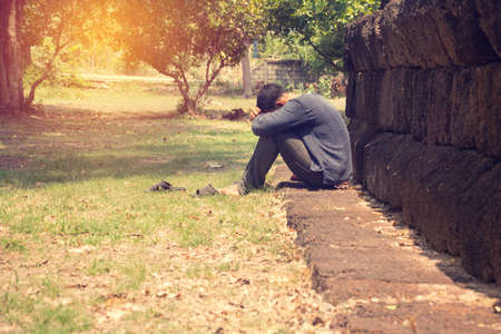 Asia you man sitting alone.He sitting alone beside old wall.man very sad and depressed.sad,alone,suicide,despair,sickness,photo health and disappointment concept.の写真素材