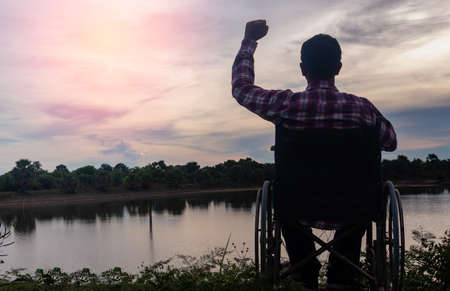 Young disabled man with river background.He is sitting on wheelchair and looking into...