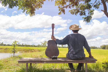Back view of relax time.A man sitting in field playing acoustic guitar and see field view.outdoor park,Musical Instrument,photo Acoustic Music and lifestyle conceptの写真素材