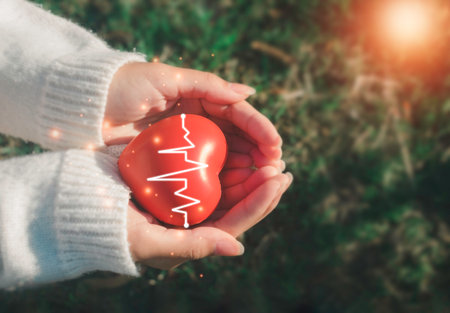 A hand holding red heart.She is Left / right hand holding it on green background.heart health,happy...