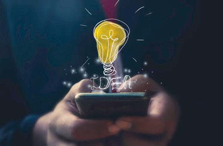 Businessman holding a smartphone with a light bulb drawing on the screenの写真素材