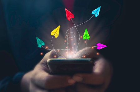 Conceptual image with flying paper planes over smartphone screen and handの写真素材