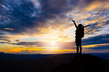 successful woman hiker open arms on top of mountain peak at sunriseの写真素材