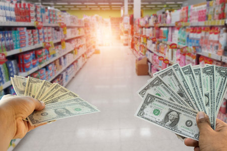 A hand holding dollars on shop. A man holding dollars for cash  on product background.Money for sales exchange. Photo concept  finances and money.の写真素材