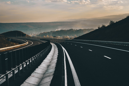Empty highway with a beautiful sunset, village and mountains in the backgroundの写真素材