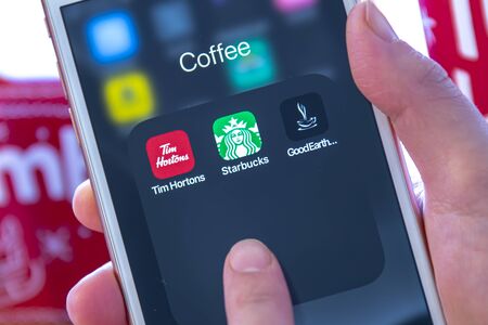 Calgary, Alberta. Canada Dec 28 2019. A person holding an iPhone looking coffee apps from Tim...