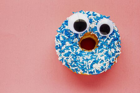 Vanilla Dip Donut with Black Wiggle Googly Eyeballs on a Coloured blue and white Sprinkles on a pink background.の写真素材
