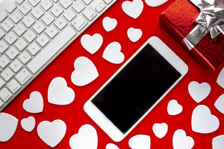 A smart phone with a keyboard a present and hearts on a red background with heartsの写真素材