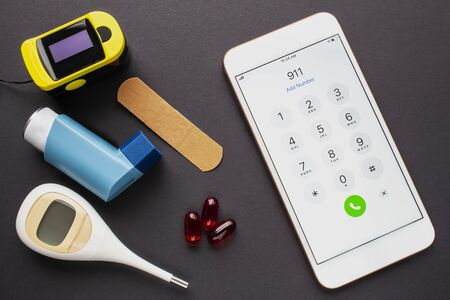 An smartphone calling the 911 dial emergency services, with an asthma inhaler, a bandage, some...