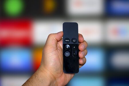 A person holding a digital media player and microconsole remote with a television screen on the...