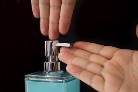 Close up of a person getting soap from a soap dispenser on a black background