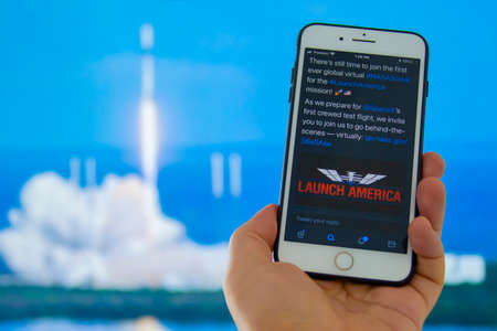 Kennedy Space Center, Florida, United States. May 27, 2020. A person holding a iPhone with the Launch America logo with an out of focus rocket launch backgroundのeditorial素材