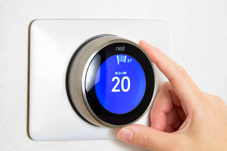 Calgary, Alberta, Canada. Jun 5, 2020. A person cooling down Home Air Conditioning, temperature is on centigrade celsius metrics using a Nest smart thermostat on a white wall.のeditorial素材