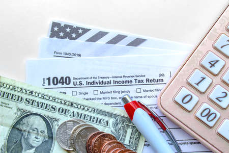 Calgary, Alberta, Canada. July 21, 2020. United States of America Tax Forms with coins, calculator, a pen on a white table. Tax time conceptのeditorial素材