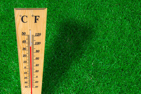 Wooden weather thermometer measurement on a green grass during a hot day.の写真素材