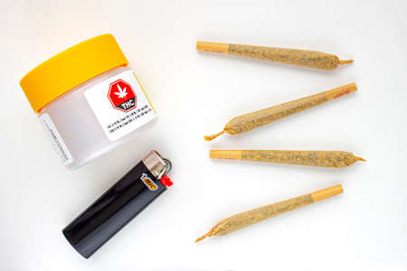 Calgary, Alberta, Canada. Aug 19, 2020. A Cannabis white and yellow plastic packaging container with Cigarettes, Prerolls or Joints and a lighter on a white backgroundのeditorial素材