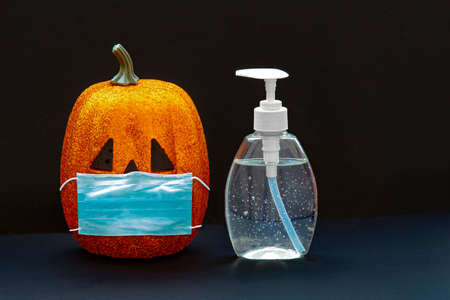Jack-o-lantern pumpkin Halloween wearing a face mask with hand sanitizer bottle on a black background. Concept: Halloween during global pandemic. Covid-19, Coronavirus.の写真素材
