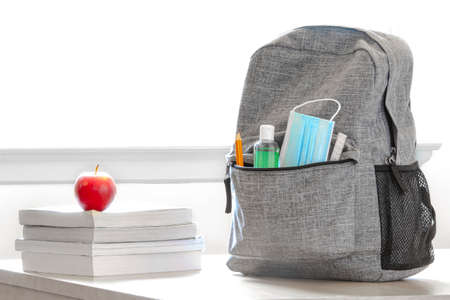 Student school bag pack with sanitizer, a face mask, pencils, books and an apple on a table. Back to...