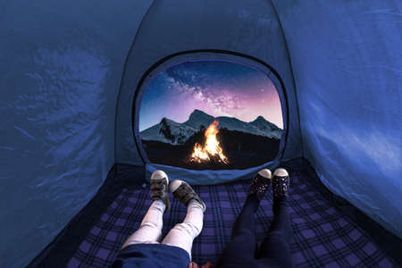 Two kids inside on a camping tent looking at the stars and mountains at night with a fire onの写真素材