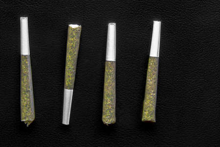 Four Pre-Roll Cannabis joints on a black leather surfaceの写真素材