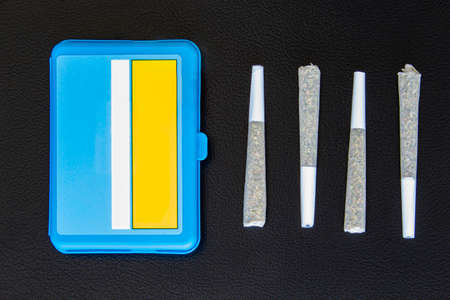 Four Joints of Legal Canadian Cannabis on a black leather background. 2 grams per joint and blue plastic case.の写真素材