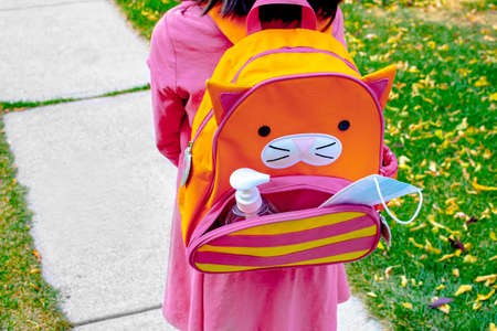 A little girl with a school bag with a face mask and hand sanitizer on a pocket