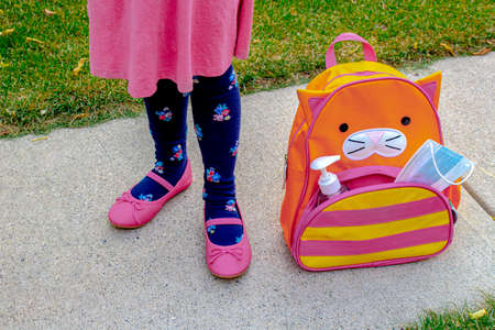 A little girl shoes next to a school bag with a face mask and hand sanitizer