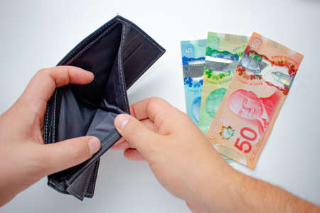 A person opening an empty wallet and spending canadian dollars on a white background. Concept:...