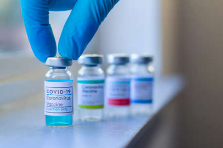 Close up of a health worker wearing globes and reaching a Covid-19 vaccine. Coronavirus vaccine or...
