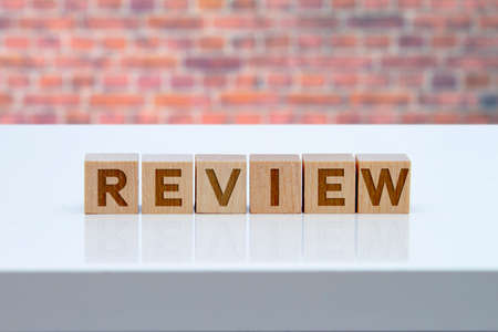 'Review' message sign on wooden blocks sitting on a white table with brink wall on the background.の写真素材