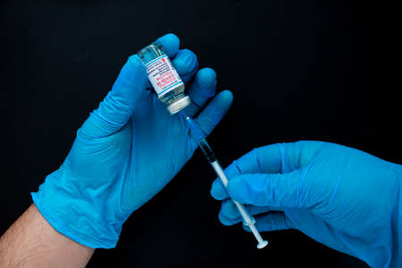 Calgary, Alberta. Canada. March 17, 2021. A health worker wearing globes with a Moderna vaccine and a syringe on a black background.のeditorial素材