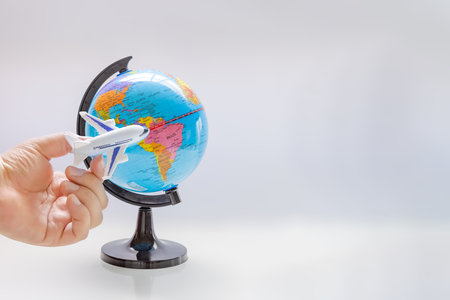 A person holding an airplane next to a world globe map sphere. Concept: International traveling.のeditorial素材