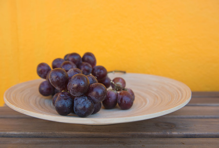 Bunch of ripe grapes in wooden plate Isolated on yellow background.の写真素材