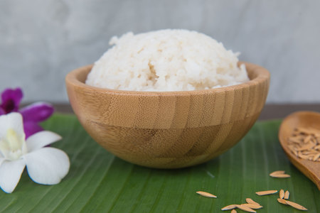 Cooked rice in bowl on green banana leaf and paddy in spoon and orchid .の写真素材