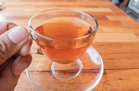 Cup hot tea in hand on the wood table background.の写真素材