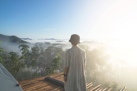 young woman standing for amazing landscape of blue sky and mountains in morning fog. Happy freedom for success and bliss concept.の写真素材