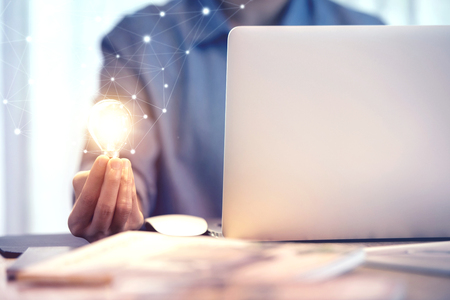 Happy woman holding light bulb while using on laptop, New ideas and creativity concept.