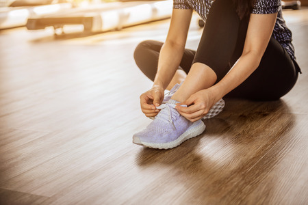 Woman tying running shoes on black floor background in gym fitness with sunlight. copy space.の写真素材
