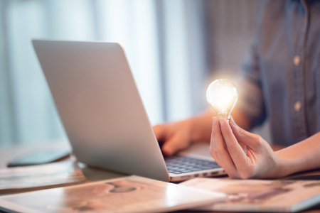 Hand holding light bulb while using on laptop, New ideas and creativity concept.の写真素材
