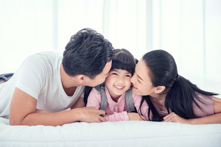 Happy Asian family, father and mother kissing daughter while smile in bedroom at home, Enjoying time together.の写真素材