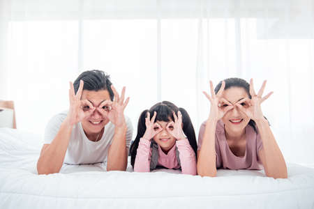 Happy Asian family (mother, father, child daughter) laying on bed while smile in bedroom at home.の写真素材