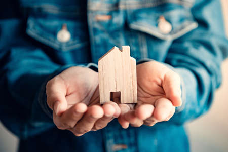 New home and real estate property concept, Woman holding wooden model house in hands.