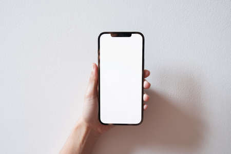 Bangkok, Thailand - Apr 10, 2021: Close up hand holding black smartphone iPhone 12 Pro Max with white screen. Isolated on white background. Mobile phone frameless design concept.のeditorial素材