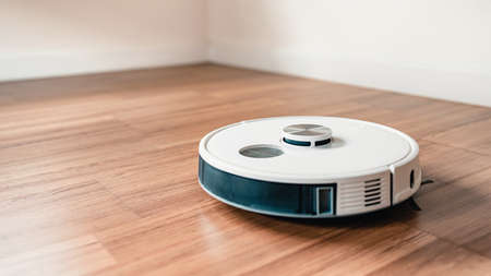 White robotic vacuum cleaner on laminate floor cleaning dust at home.の写真素材