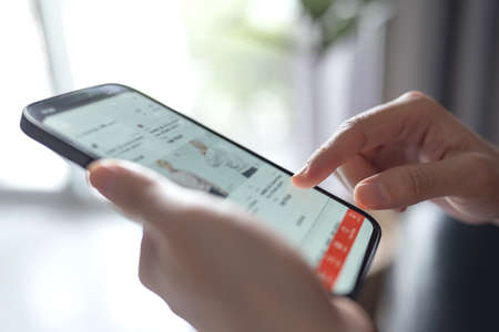Woman online shopping on smart phone fashion clothes at homeの写真素材
