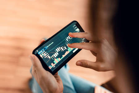 Closeup - Woman is checking Bitcoin price chart on digital exchange on mobile smartphone,...