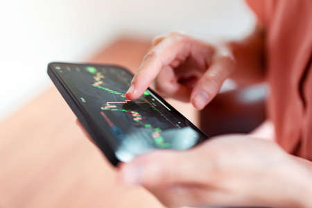 Closeup - Woman is checking Bitcoin price chart on digital exchange on mobile smartphone, cryptocurrency future price action prediction.の写真素材
