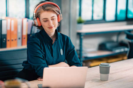 Happy woman wearing headphones and holding video call with clients on laptop at office. consulting customer.の写真素材