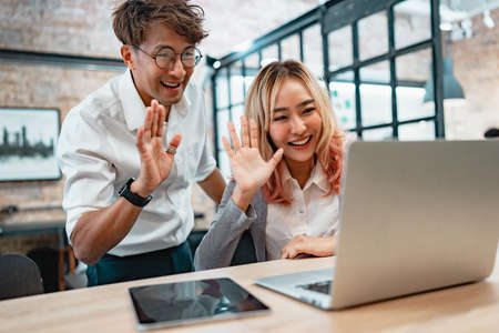 Happy man and woman waving hand looking at screen at web camera greeting, Smiling young couple making distance video call on laptop at cafeの写真素材